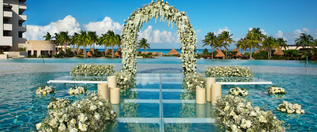 Destination wedding, wedding venue set up over a pool, flower arch, candles, elegant wedding setting, beach view