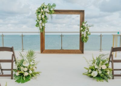 Square wedding arch with white floral bouquets set up at the beach for a destination wedding.