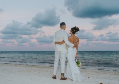 back view of couple looking out at the beach clouds at sunset.