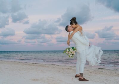 couple kissing at the beach, groom is lifting up his bride.