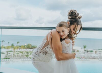 adult hugging child, bridal party. hotel pool and beach scene can be seen in the background.