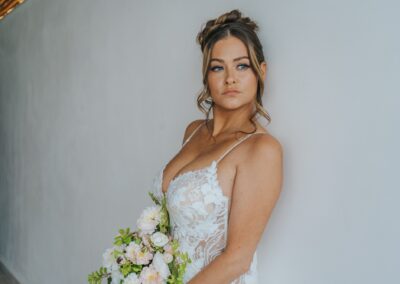 bride wearing a gown and holding a bridal bouquet for her destination wedding. White wall in the background.